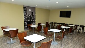 A dining area with multiple tables and chairs, a cityscape mural on the wall, and a flat-screen TV mounted on the wall.