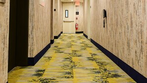 A hotel corridor with a patterned carpet, wooden walls, and a fire extinguisher on the wall.