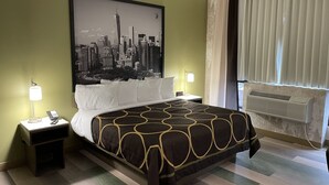 A hotel room with a bed, two bedside tables, a cityscape wall art, a window with curtains, and an air conditioning unit.