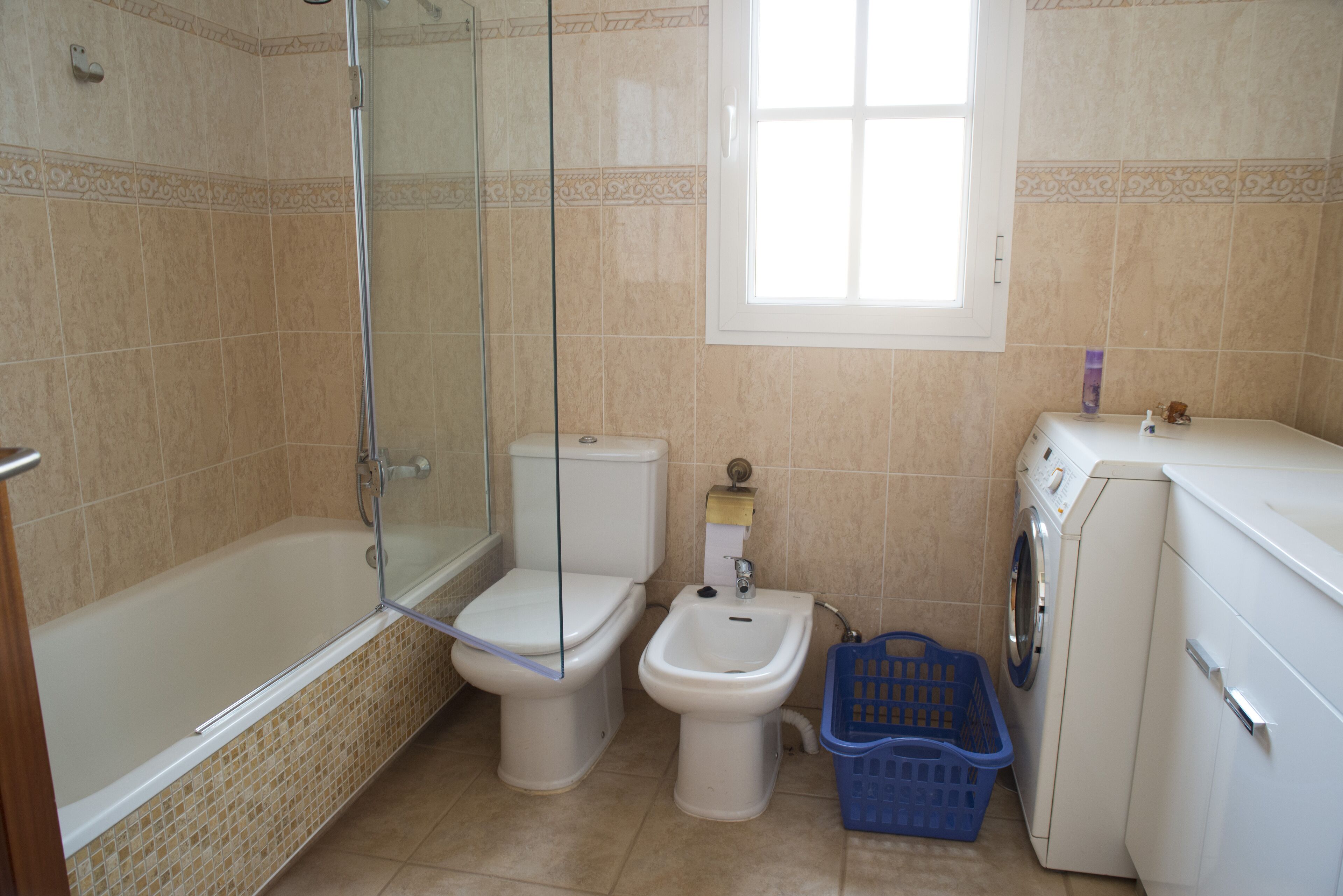 A bathroom with a glass-enclosed shower, a toilet, a bidet, and a washing machine.