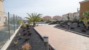 Un camí pavimentat amb una piscina, envoltat per una tanca i diferents plantes.