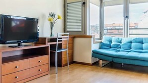 A living room with a TV, a desk, a chair, a sofa, and a window with a view of buildings. - Bright Quiet Flat | Terrace by HostWise (Porto)
