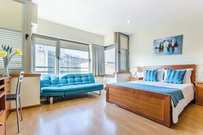 Un dormitorio moderno con una cama grande, un sofá azul y vistas a la ciudad a través de amplias ventanas.