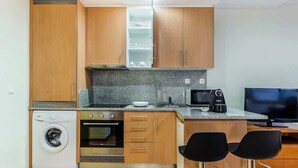 A compact kitchen with wooden cabinets, a built-in oven, a microwave, a washing machine, and two black bar stools. - Bright Quiet Flat | Terrace by HostWise (Porto)