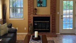 Una sala de estar con chimenea, ventilador de techo y puerta que da al exterior.