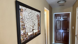 Un pasillo con una obra de arte abstracta enmarcada en la pared, una puerta de madera y un suelo de baldosas.