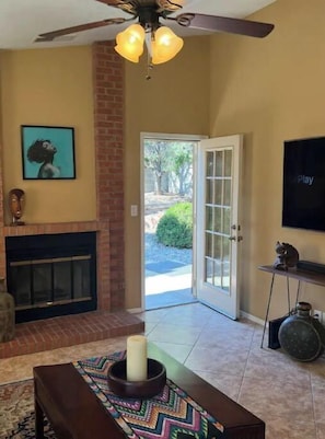 Una sala de estar con chimenea, ventilador de techo, televisor y puerta que da al exterior.
