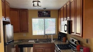Una cocina compacta con armarios de madera, un refrigerador de acero inoxidable, un microondas, una estufa y un lavamanos.