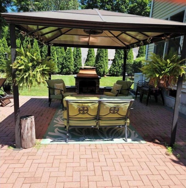 Relax by the stone fireplace in this serene outdoor space surrounded by lush greenery and comfortable seating.