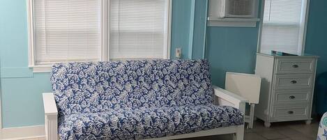 A room with a blue sofa, white dresser, and a window with blinds.