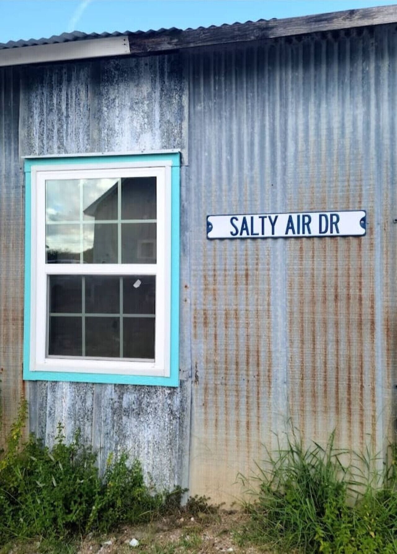 A corrugated metal building with a window and a street sign reading "SALTY AIR DR".