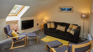A cozy living room with a black sofa, two armchairs, a small table, a TV, and a skylight. - Campbells Loft (Oban)