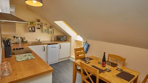 A compact kitchen with a dining area, featuring a wooden table, chairs, and a small dining set. - Campbells Loft (Oban)