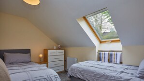 A bedroom with two beds, a dresser, a nightstand, a radiator, and a skylight. - Campbells Loft (Oban)