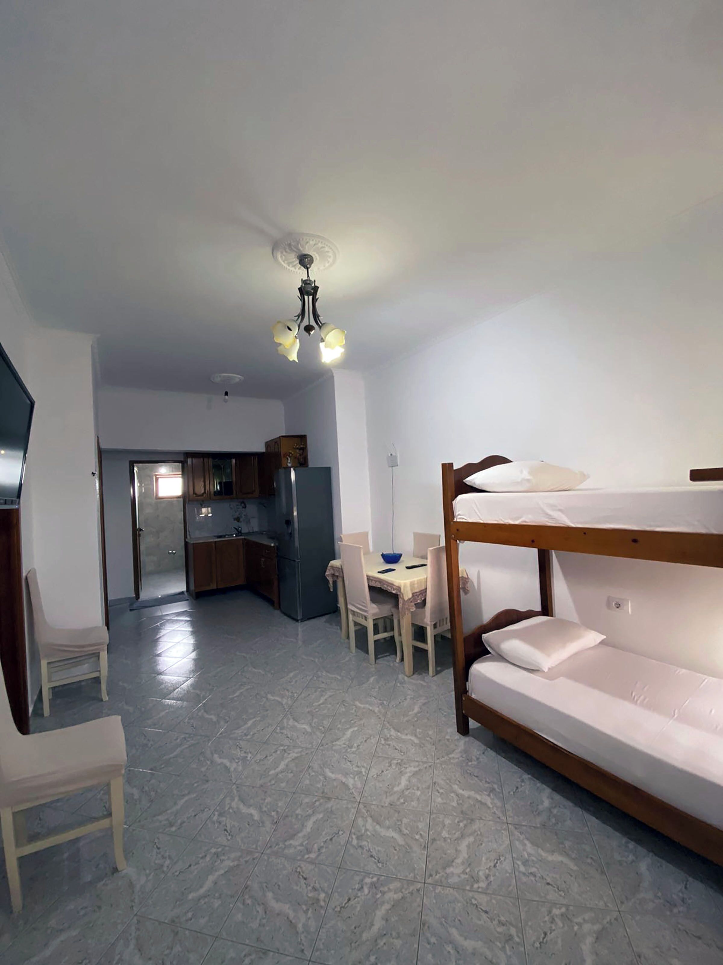 A compact room with a bunk bed, a dining table with chairs, a kitchen area, and a ceiling light fixture.