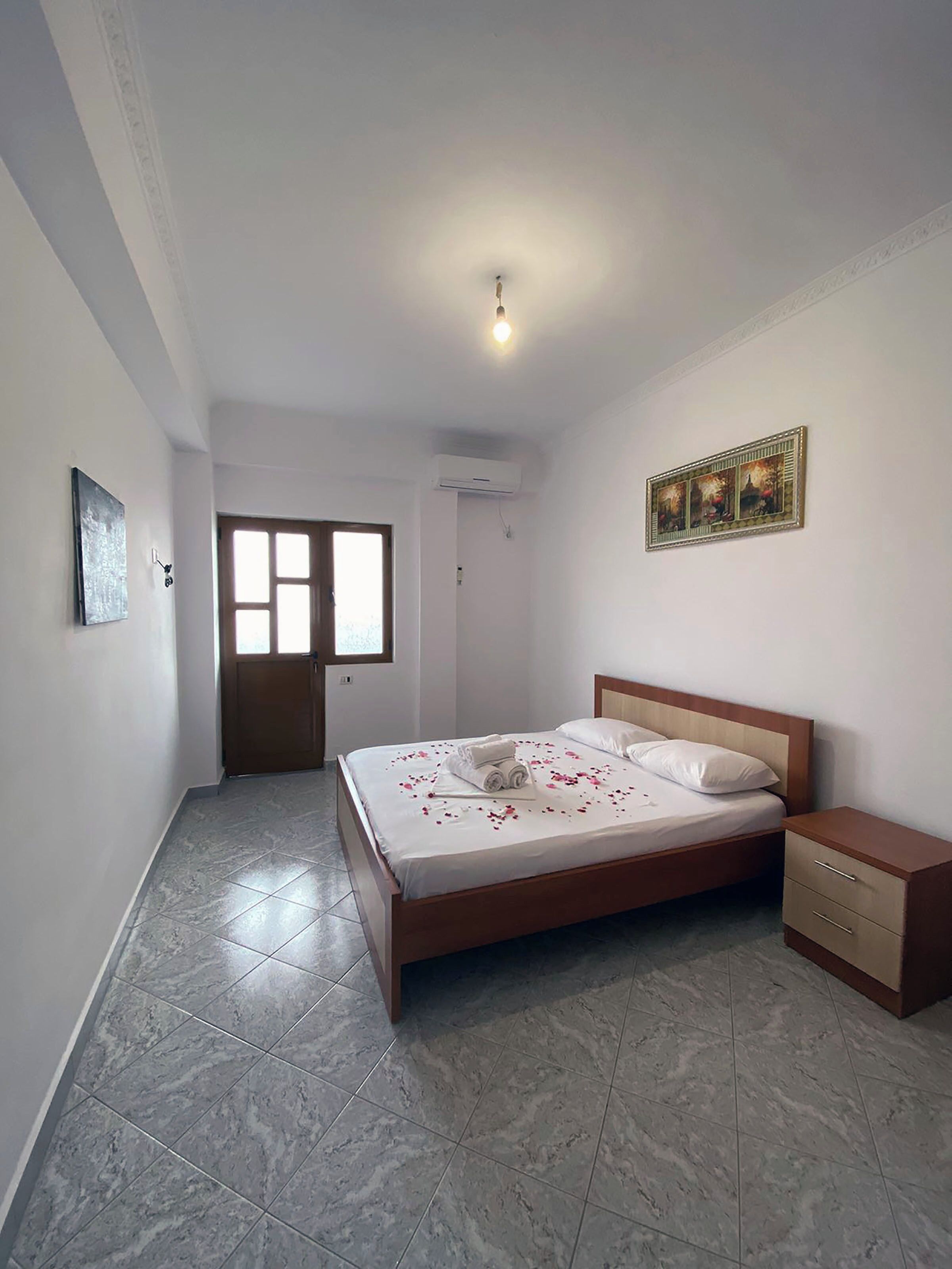 A bedroom with a bed, a nightstand, a door, and a window.