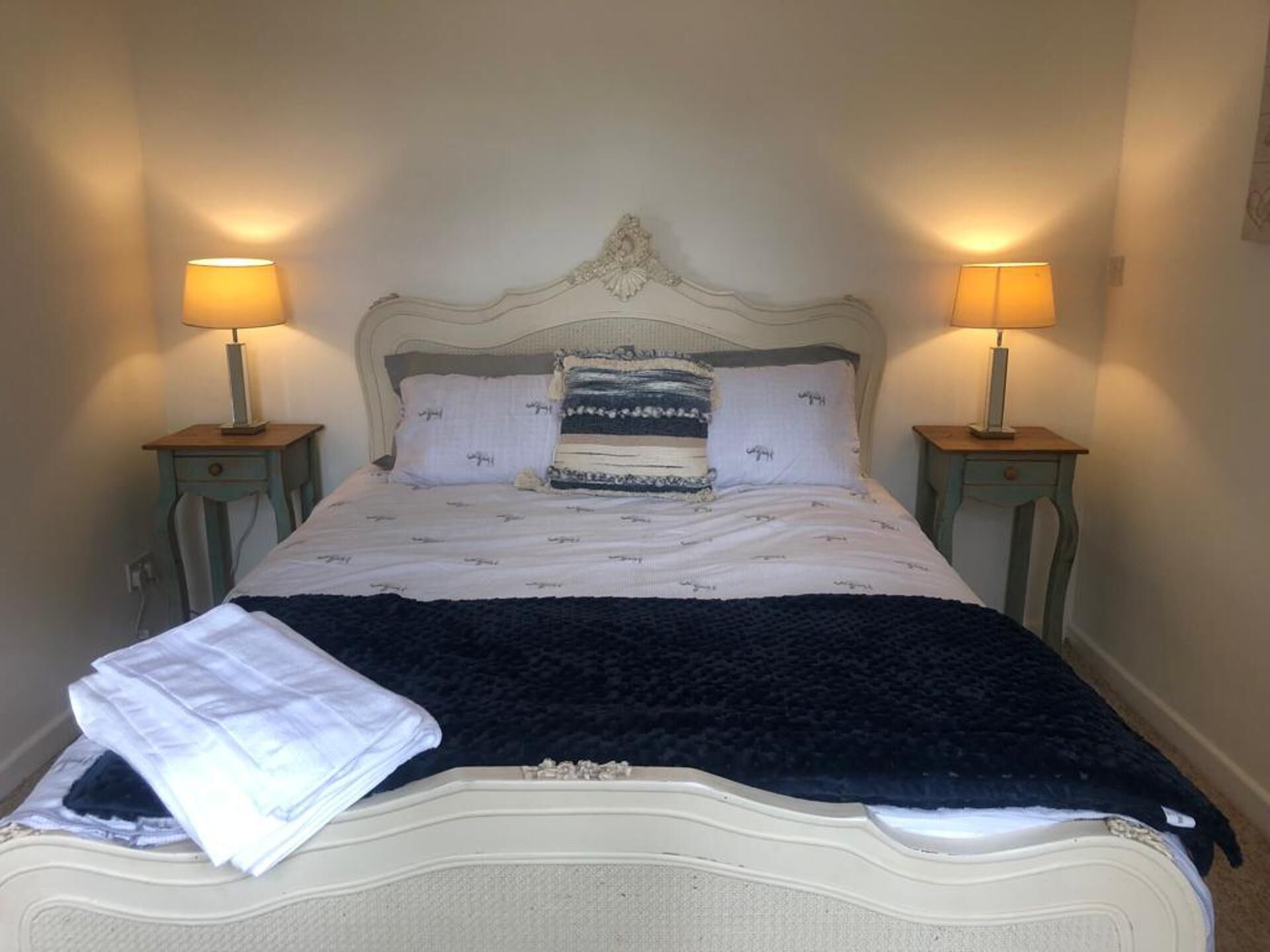 A neatly made bed with a patterned pillow, two bedside lamps, and a folded blanket on the bed.