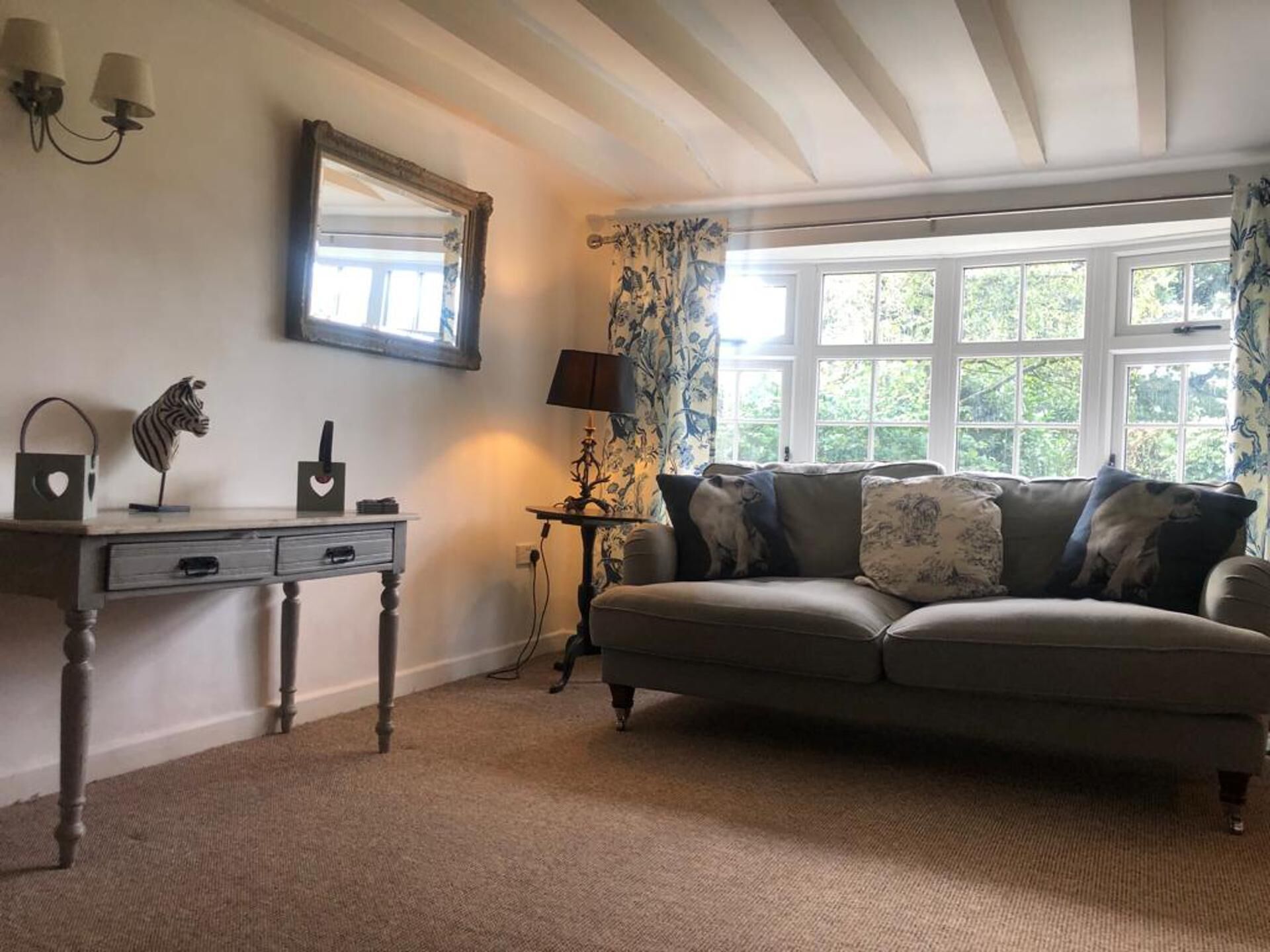 A cozy living room with a sofa, a small table, a lamp, and a decorative mirror.