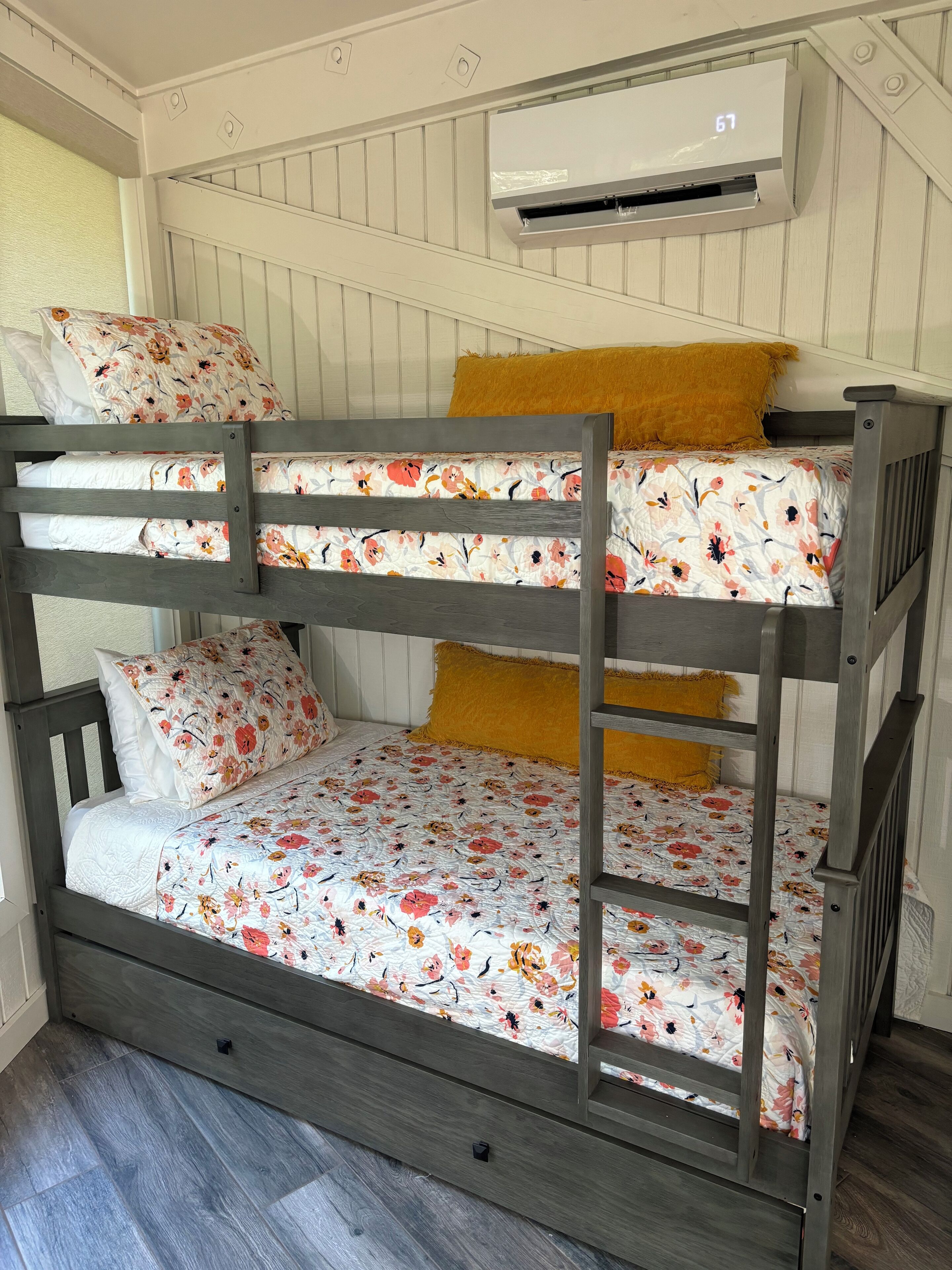 A bunk bed with floral bedding, a wooden headboard, and a ceiling-mounted air conditioner.