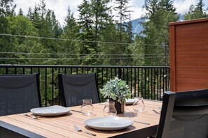 An outdoor dining table with chairs, a potted plant, and a view of a forest and mountains.
