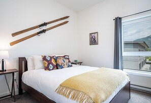 A bedroom with a bed, a window, a desk, and a wall-mounted ski rack.