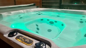 A hot tub with control panel and jets, set against wooden paneling and a glass partition.