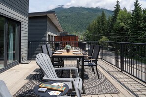 A deck with a table and chairs, overlooking a forested mountain range.