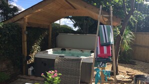 A hot tub under a wooden pergola, surrounded by greenery and a table with drinks and a candle. - Stunning 1-bed Cottage With Hot Tub in Ross-on-wye (Ross-on-Wye)