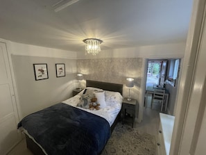 Quarto com cama, luminárias de cabeceira, um candelabro e uma escrivaninha com cadeira.