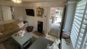A living room with a sofa, a coffee table with flowers, a fireplace, and a television. - Stunning 1-bed Cottage With Hot Tub in Ross-on-wye (Ross-on-Wye)