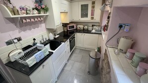 A compact kitchen with white cabinets, a black countertop, a sink, a trash bin, and a microwave. - Stunning 1-bed Cottage With Hot Tub in Ross-on-wye (Ross-on-Wye)