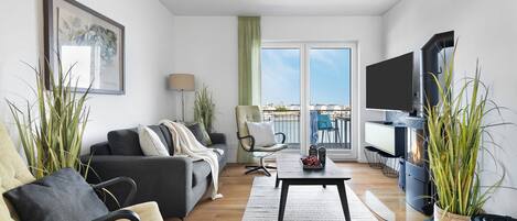 Ein modernes Wohnzimmer mit Sofa, Sessel und Couchtisch, einem Flachbildfernseher und einem Kamin.