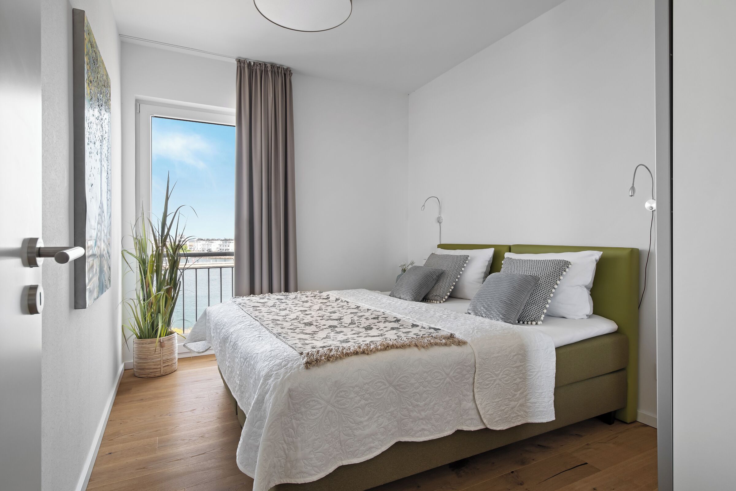 A bedroom with a bed, a window, a plant, and a view of the sky.