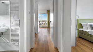 Une chambre d’hôtel avec un plancher en bois, un canapé vert, un lit blanc et une vue sur la ville depuis un balcon.