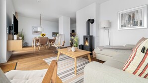 Una sala de estar moderna con sofá, mesa de centro y chimenea. En el fondo, hay un comedor con mesa y sillas.