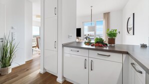 A modern kitchen with white cabinets, a grey countertop, and a view of the city. - "Ocean Waves" Baltic Sea vacation with a 3-minute walk to the beach, fireplace and sea view (Olpenitz)