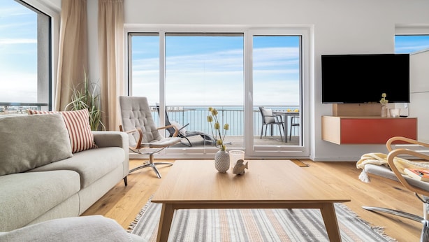 A modern living room with a sofa, armchair, coffee table, and a flat-screen TV. - "Ocean Waves" Baltic Sea vacation with a 3-minute walk to the beach, fireplace and sea view (Olpenitz)
