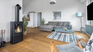 Ett modernt vardagsrum med en vedkamin, en grå soffa, ett blått soffbord och en randig matta.