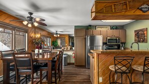 A modern kitchen with wooden cabinets, a stainless steel refrigerator, and a dining area with a wooden table and chairs. - Close to the Slopes! Pool & Hot Tubs! Winter Shuttle! (Steamboat Springs)