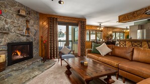 A cozy living room with a stone fireplace, leather sofa, wooden coffee table, and a view of the snowy outdoors through large windows. - Close to the Slopes! Pool & Hot Tubs! Winter Shuttle! (Steamboat Springs)