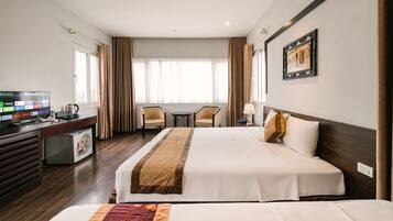 A hotel room with a bed, desk, TV, chairs, and a window.
