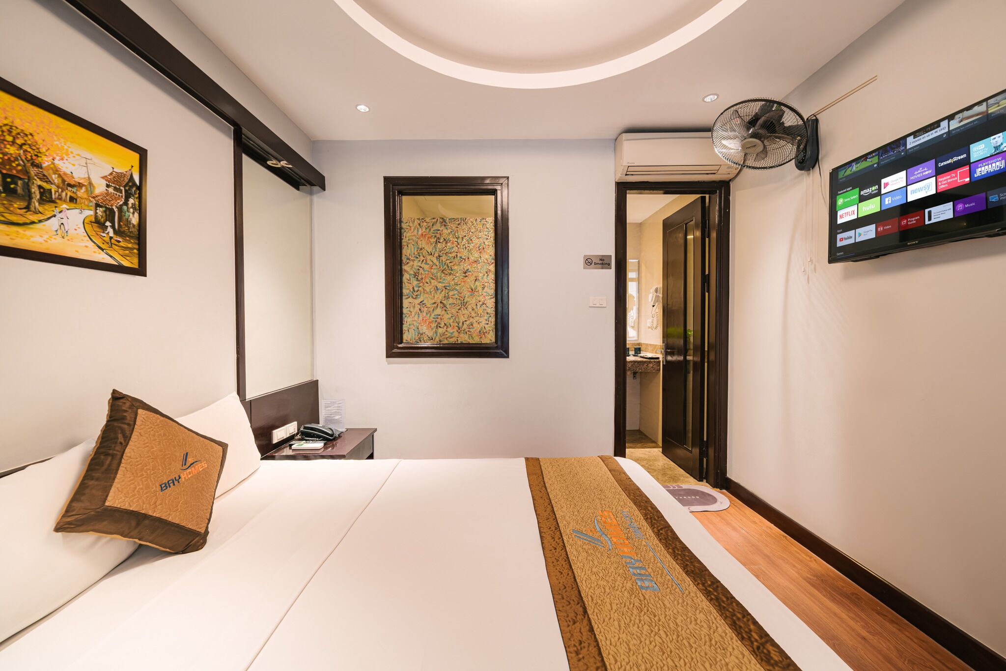 Ein Hotelzimmer mit einem Bett, einem an der Wand montierten Fernseher, einem Bild an der Wand und einer Tür zu einem Badezimmer.