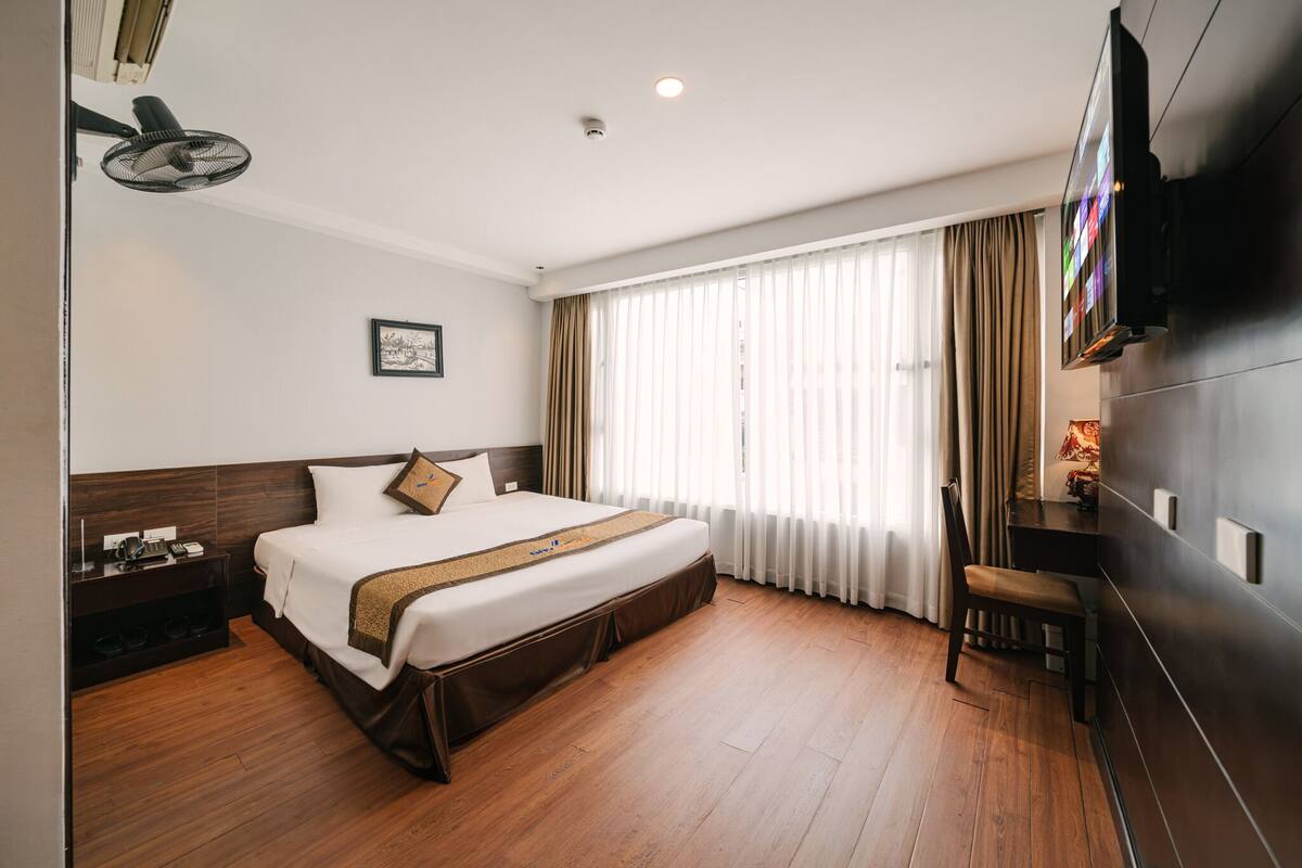 Een hotelkamer met een bed, een bureau, een stoel, een televisie en een raam met gordijnen.