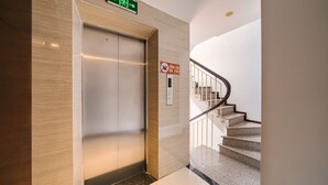 Ein Aufzug mit einem grünen Ausgangsschild, einem Feuermelder und einer Treppe mit Handlauf.