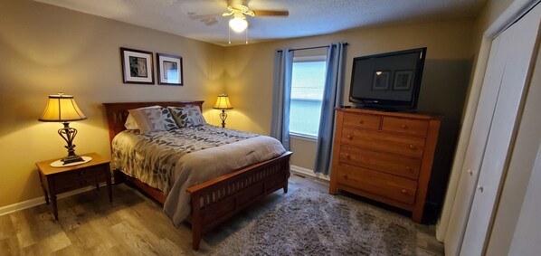 Une chambre à coucher comprenant un lit, deux lampes de chevet, une commode, un téléviseur et un ventilateur de plafond.