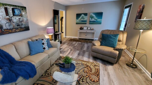 Un salon avec un canapé beige, un plaid bleu, une table basse ornée d’une plante et un tapis à motifs.