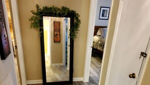 Un couloir doté d’un plancher en bois, d’un miroir et d’une porte donnant sur une chambre à coucher.