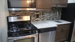 Una cocina con estufa, horno y lavavajillas de acero inoxidable, encimera de granito y armarios de madera.