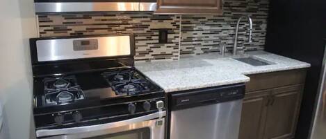 A kitchen with a stainless steel stove, oven, and dishwasher, a granite countertop, and wooden cabinets.