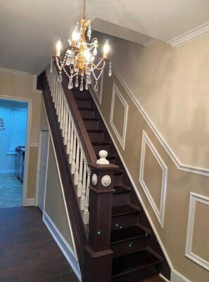 A staircase with dark wood railings and white balusters, leading to a room with a chandelier.